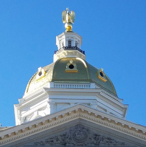Close-up of a golden dome topped with an eagle statue against a clear blue sky.