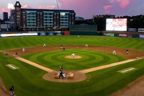 A baseball field at sunset with players in action and a stadium in the background.