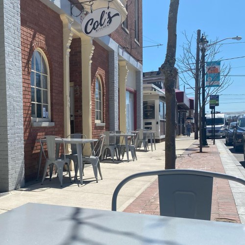 Outdoor seating area in front of Col's Kitchen, with tables and chairs along a sunny street.