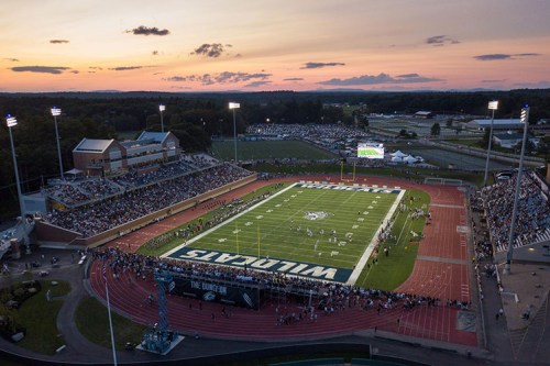 Aerial view of a packed stadium at sunset, featuring a football field and surrounding track.