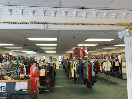 Interior of a thrift store with rows of clothing racks and colorful decorations along the ceiling.