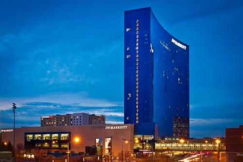 A tall, modern JW Marriott hotel illuminated at dusk, with a clear blue sky and city lights in the foreground.