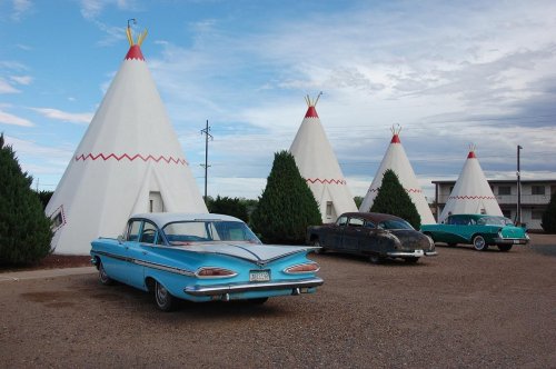 Vintage cars parked in front of iconic teepee-shaped structures under a cloudy sky.