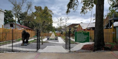 A mini-golf course with a statue, surrounded by trees and a fence, under a cloudy sky. Course rules sign visible.