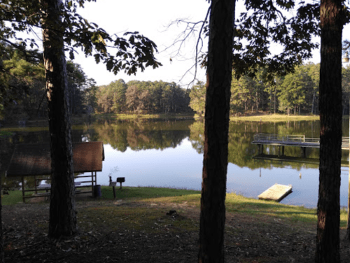 A serene lake surrounded by trees, with a small cabin and dock visible on the shore.