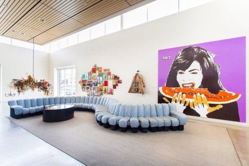 A modern lounge area featuring a curved blue sofa, a round table, and vibrant wall art, including a large mural of a woman.