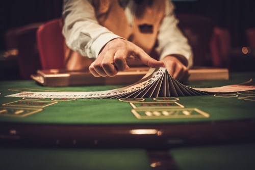 A dealer shuffles a deck of cards on a green casino table, with chips and game markings visible.