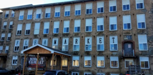 Exterior of a large, weathered building with "FLEA MARKET" painted on the facade and a sign for "Mission Company" below.