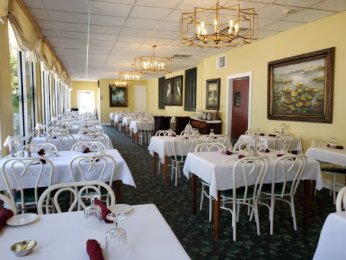 Brightly lit restaurant interior with white tablecloths, elegant chandeliers, and artwork on yellow walls.