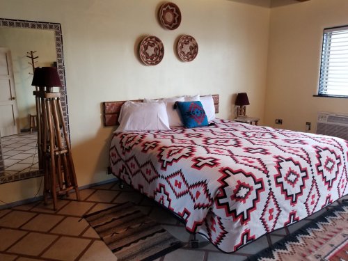 Cozy bedroom featuring a patterned bedspread, wooden decor, and a mirror, with warm lighting and earthy tones.