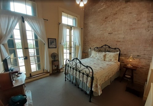 Cozy bedroom with a wrought iron bed, large windows, and exposed brick walls, featuring soft lighting and a warm atmosphere.