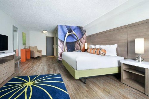 A modern hotel room featuring a large bed, colorful decor, a TV, and a cozy seating area.