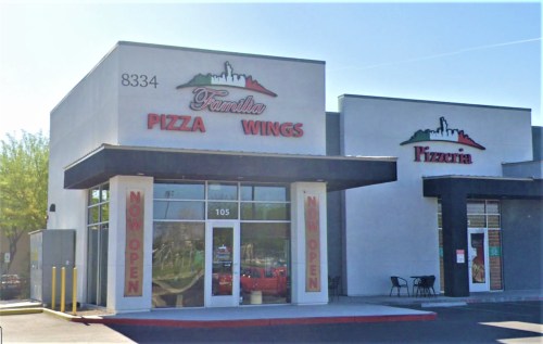 Exterior of a pizza restaurant named "Familia Pizza Wings," featuring a bright sign and "Now Open" banners.
