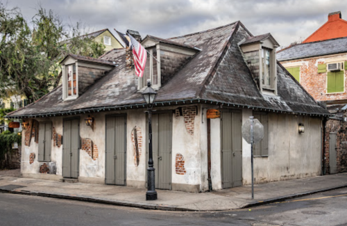 Historic building with a sloped roof, weathered walls, and an American flag, set on a quiet street.