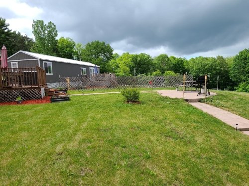 A grassy yard with a patio, picnic table, and a mobile home in the background under a cloudy sky.