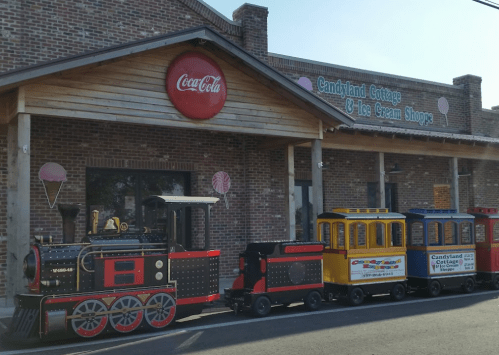 A colorful toy train in front of a brick building with a sign for Candyland Cottage & Ice Cream Shops.
