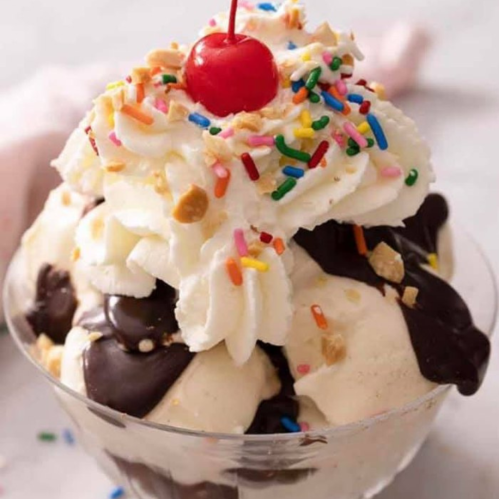 A delicious ice cream sundae topped with whipped cream, chocolate sauce, sprinkles, and a cherry.