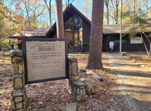 A wooden welcome sign at the entrance of a nature park, surrounded by trees and autumn leaves.