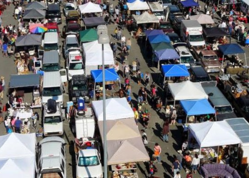 Aerial view of a bustling outdoor market with numerous tents, vehicles, and crowds of people browsing.