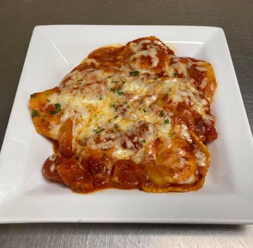 A plate of cheesy pasta in marinara sauce, garnished with herbs, served on a white square dish.