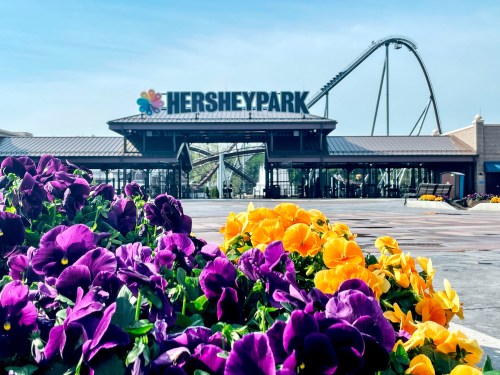 Entrance to Hersheypark with colorful flowers in the foreground and a roller coaster in the background.