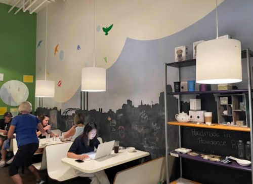 A cozy café interior with colorful wall art, tables, and customers enjoying coffee and working on laptops.