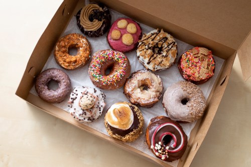 A box filled with a variety of colorful donuts, including sprinkles, chocolate, and cream-filled options.