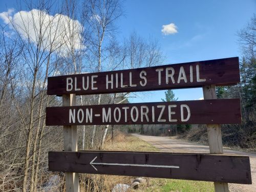 Sign for Blue Hills Trail, indicating it's non-motorized, with a dirt path and trees in the background.