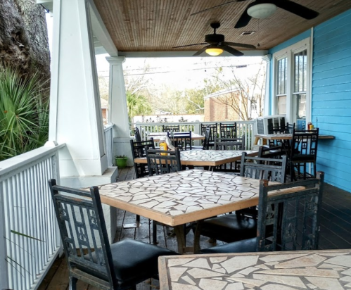 Outdoor dining area with mosaic tables and black chairs, surrounded by greenery and a blue wall.