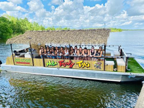 A group of people on a boat with a thatched roof, enjoying a sunny day on the water surrounded by greenery.