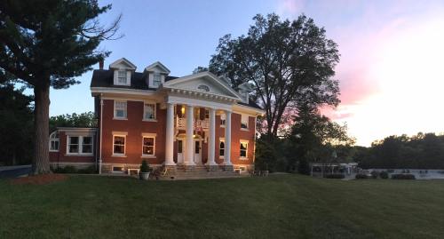 A large red brick mansion with white columns, surrounded by trees, at sunset with a colorful sky.