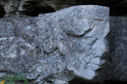 Carved stone sculpture of a face, partially weathered, set against a rocky background.