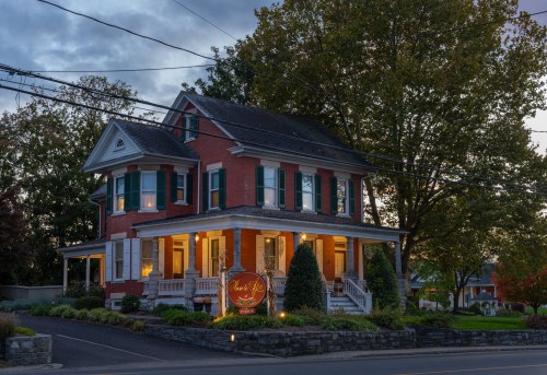 A charming brick house with green shutters, illuminated at dusk, featuring a sign that reads "Uncle Ray's."