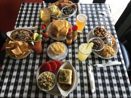A table set with various dishes, including nachos, cornbread, salads, and drinks, on a checkered tablecloth.