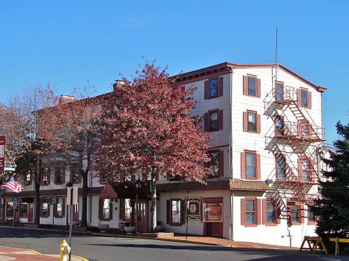 Historic building with a white facade, red accents, and a fire escape, surrounded by trees and a clear blue sky.