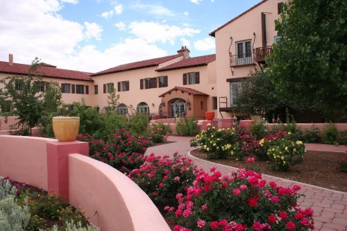 A charming building surrounded by vibrant rose gardens and lush greenery under a blue sky with scattered clouds.