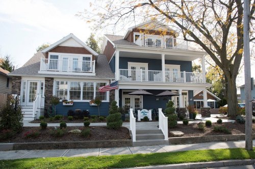 A charming two-story house with a blue exterior, white railings, and a front porch, surrounded by landscaped greenery.