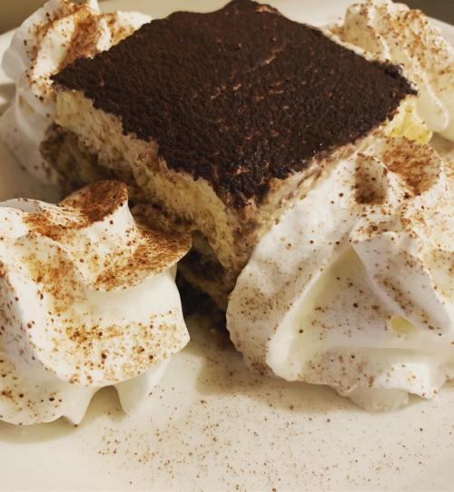 A slice of dessert topped with cocoa powder, surrounded by dollops of whipped cream.