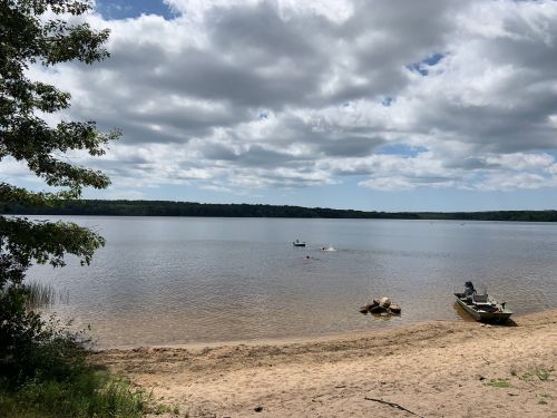 A serene lakeside view with sandy shore, boats on the water, and cloudy skies above.