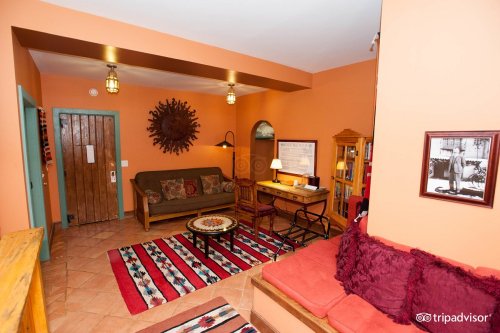 Cozy living room with orange walls, a wooden door, seating, a desk, and decorative rugs. Warm and inviting atmosphere.