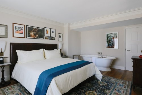 A modern bedroom featuring a large bed, artwork on the walls, and a freestanding bathtub in the corner.