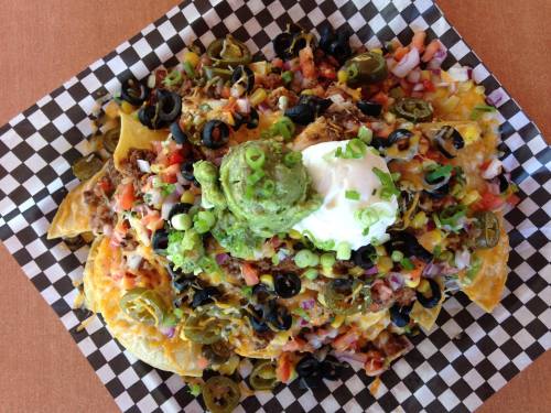 A plate of loaded nachos topped with cheese, jalapeños, olives, guacamole, sour cream, and diced vegetables.