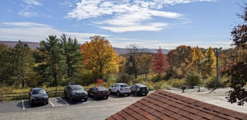 A scenic view of colorful autumn trees and a parking lot with several cars under a clear blue sky.