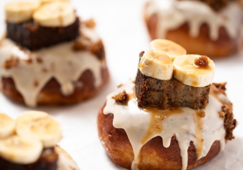 Delicious donuts topped with creamy glaze, banana slices, and a piece of cake, garnished with crumbs.