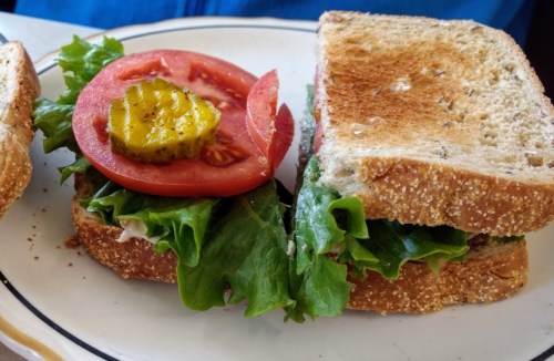 A close-up of a sandwich with lettuce, tomato, and a pickle slice on toasted whole grain bread.