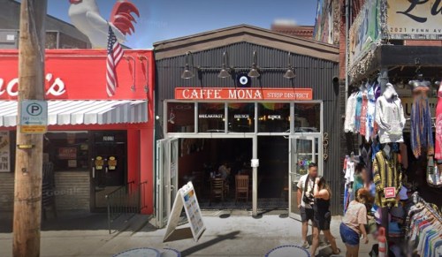 A café with a red sign reading "Caffe Mona" in a vibrant street market, surrounded by colorful shops and people.