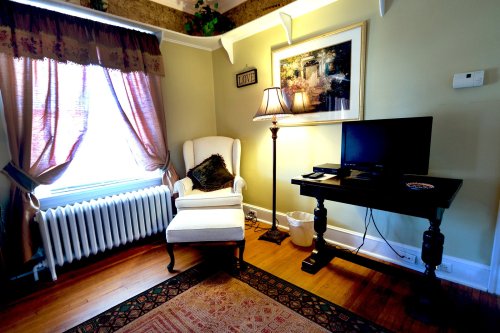 Cozy room featuring a white armchair, lamp, TV on a table, and a window with curtains, creating a warm atmosphere.