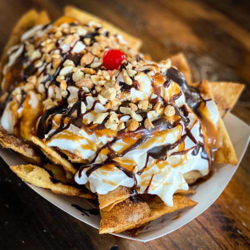 A dessert bowl filled with crispy tortilla chips, topped with ice cream, whipped cream, nuts, chocolate, and a cherry.