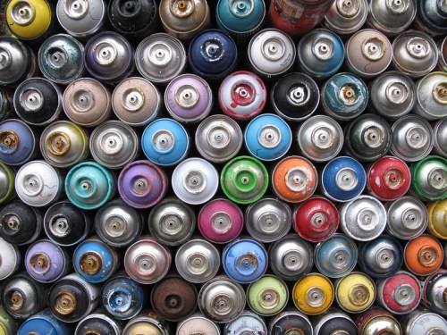 A close-up view of numerous spray paint cans stacked closely together, showcasing a variety of colors and textures.
