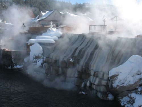 Steam rises from a snow-covered cliff near a building, creating a mystical winter landscape.